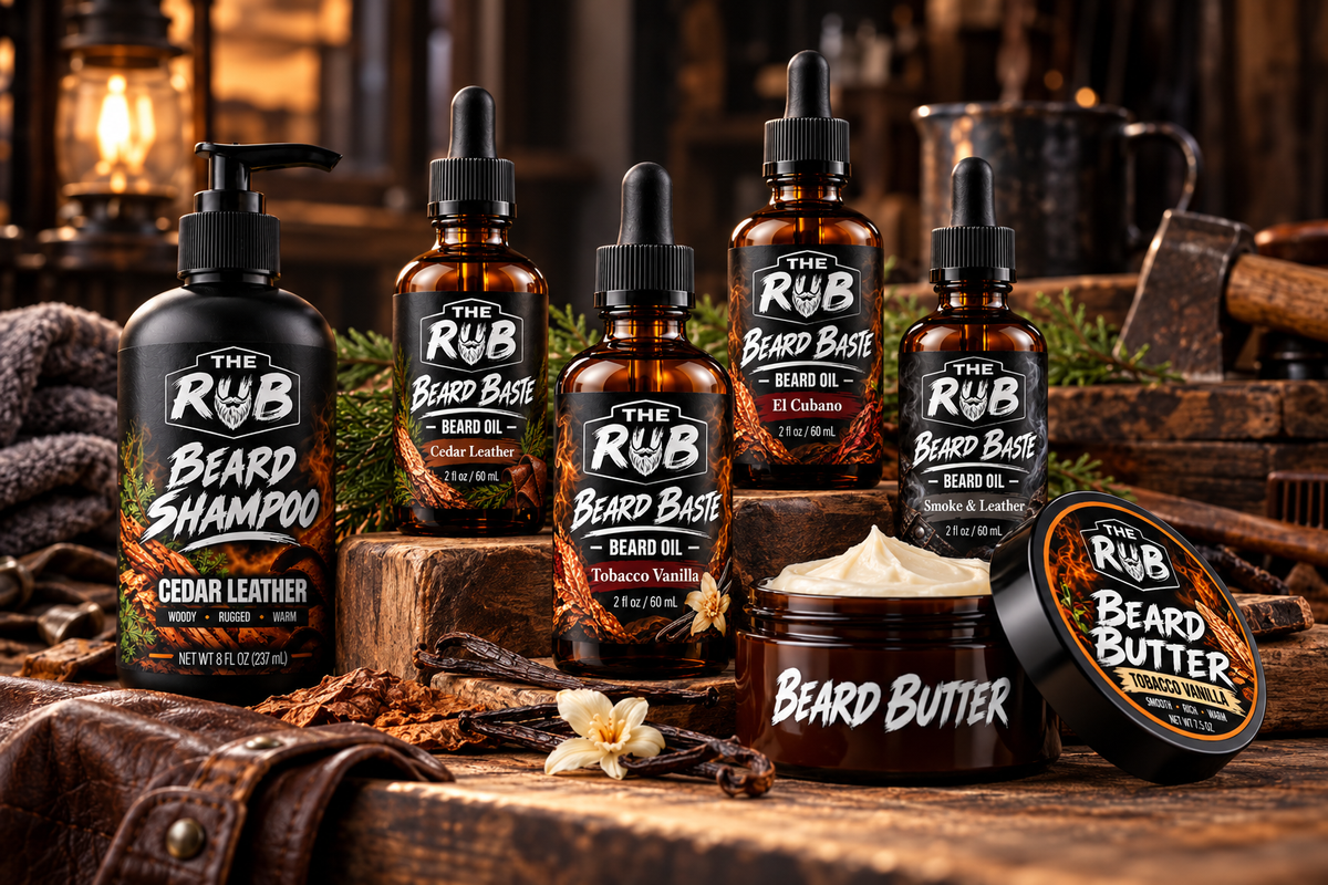 The Rub Beard Care Collection featuring Beard Baste beard oils in Cedar Leather, Tobacco Vanilla, El Cubano, and Smoke & Leather, plus Beard Shampoo and Beard Butter, displayed on a rugged wooden barbershop workbench.