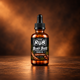 The Rub Beard Baste Cedar Leather Beard Oil – 2 oz amber glass dropper bottle featuring a rugged cedarwood and leather-inspired label against a warm, woodsy background.