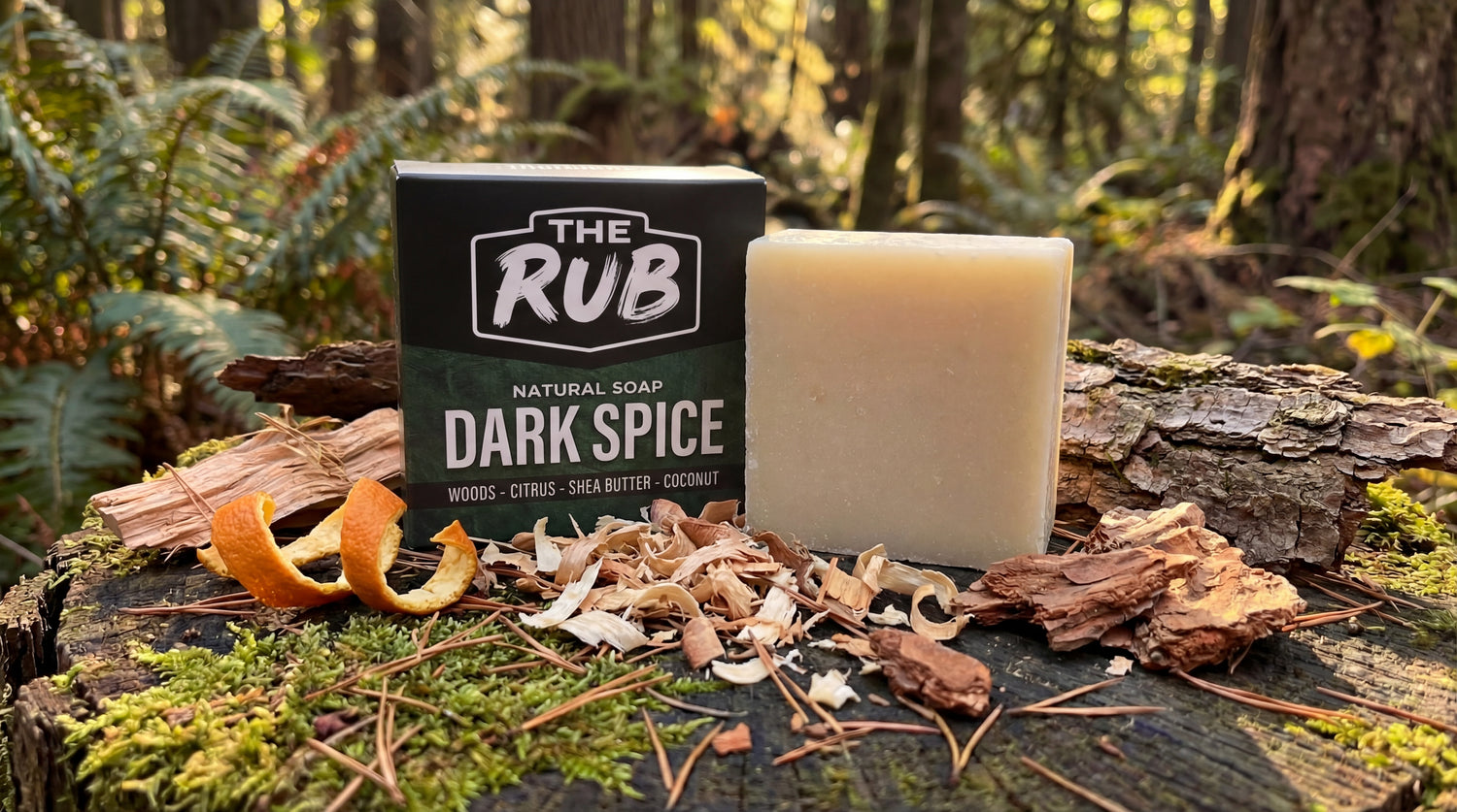 Dark Spice natural soap bar and box by The Rub on a mossy outdoor stump with wood bark and orange peel accents.