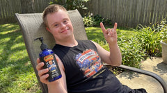 Drew from @down.rightdelicious lounging outdoors holding a bottle of his Wash My Damn Hands liquid soap.