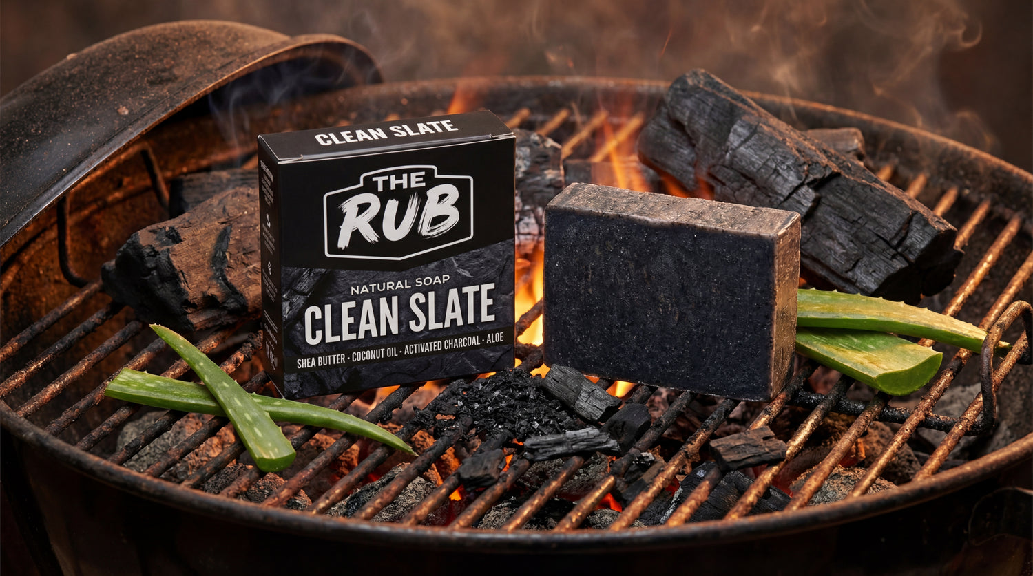 Clean Slate natural soap bar and box by The Rub on a smoking charcoal grill with aloe vera leaves and burning embers.