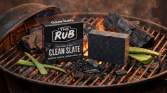 Clean Slate natural soap bar and box by The Rub on a smoking charcoal grill with aloe vera leaves and burning embers.