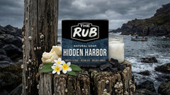 Hidden Harbor natural bar soap by The Rub on weathered ocean pylons with tropical flowers, charcoal, and a rocky coast.