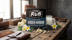 Hidden Harbor natural bar soap by The Rub on a craftsman’s wooden workbench with raw shea butter and tropical plumeria.