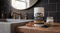 Smooth Cedar natural deodorant by The Rub on a wooden bathroom vanity next to a concrete sink and raw ingredients.